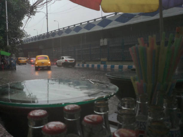 Kolkata, West Bengal, India - 16th August 2019 : A roadside shop is being wet under monsoon raining, waterlogged road in the backgrounnd. Yellow taxi waiting . Rainy season of Kolkata, stock photo