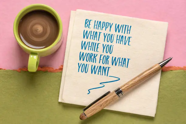 be happy with what you have whole you work for what you want - inspirational message on a napkin with a cup of coffee, minimalism and personal development concept