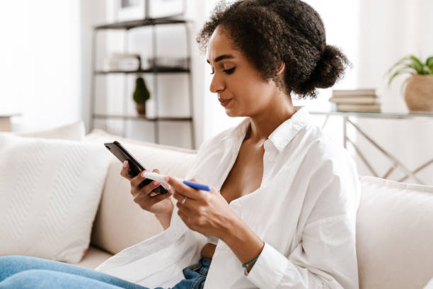 istock Young black woman holding pregnancy test and using cellphone 1450351585