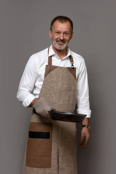 istock A man in a linen kitchen apron is holding a cast-iron pan with a pot holder. 1450351679