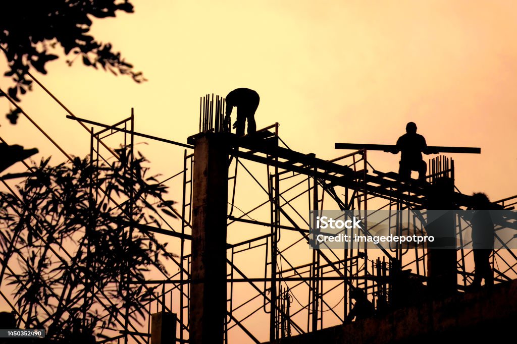 Silhouetted construction workers in construction site Construction workers in construction site over sunset Stability Stock Photo