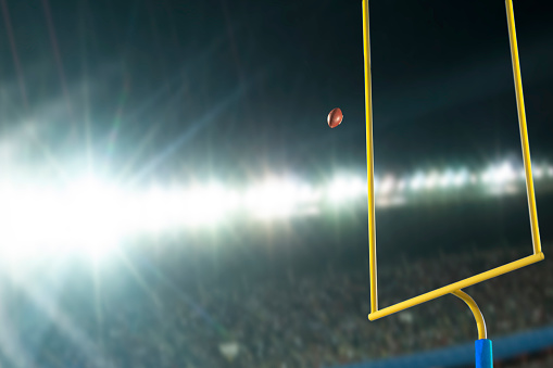 Making a field goal or extra point through the goal post during an American football game at night in stadium with lens flare from the lights.