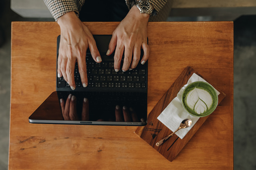 Focused business woman working on a laptop computer while sitting in a cafeteria and drinking coffee.