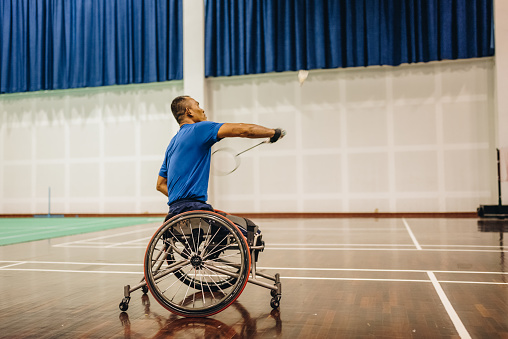 Male disabled badminton player competes with his teammates on the badminton court. while sitting in a wheelchair.