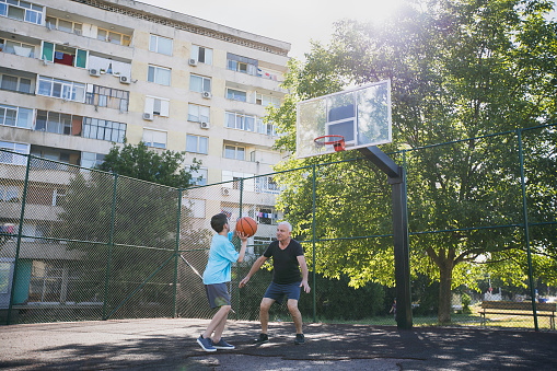 Happy grandfather and grandson practicing basketball.
