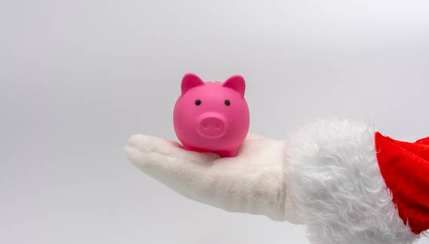 Santa's hand holds a piggy bank in the palm of his hand stock photo