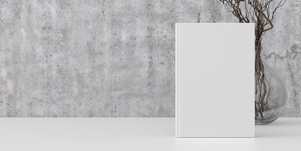 Vertical book cover mock up standing on a white desk with concrete wall background. 3d illustration