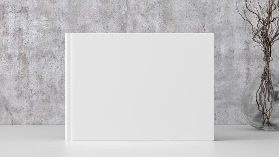 Horizontal book cover mock up standing on a white desk with concrete wall background.