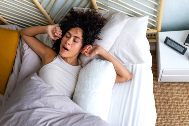 young african american woman waking up in the morning, yawning and stretching arms in bed. good morning. - wake up stretching women black imagens e fotografias de stock