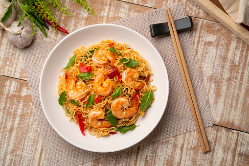 Spicy stir fried instant noodle with shrimps and thai basil leaves in white plate.Top view