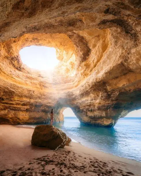 A vertical shot of a person standing on the rock, Benagil cave in Algarve, Portugal