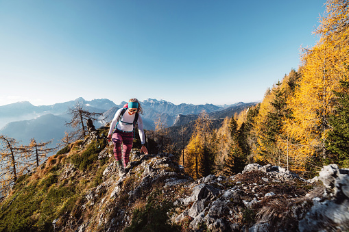 Scenic view of autumn mountain, European Alps, from a view point, where caucasian woman hiker is standing. Sun is shining high up in the mountains, a light mist in the valleys down bellow. Woman mountaineer enjoying the view of majestic Alps on a sunny autumn day.