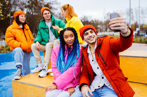 Multiracial group of young happy friends meeting outdoors in winter, wearing winter jackets and having fun, couple taking selfie on smartphone for social media - Multiethnic millennials bonding in a urban area, concepts about youth and social releationships