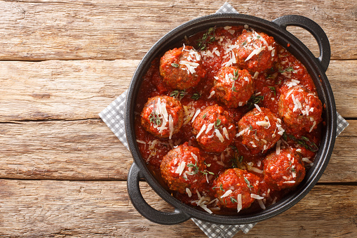 Polpette meatballs with parmesan stewed in a rich tomato sauce close-up in a frying pan on the table. Horizontal top view from above