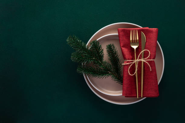 istock Christmas or New Year dinner table setting with empty plate and golden cutlery on dark green background, card or menu template with fir tree. Copy space, flat lay design. Top view. Winter holidays. 1450377650