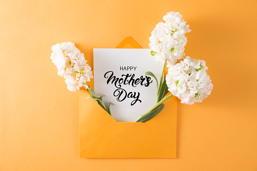 Flowers in yellow envelope with mothers day greeting card on yellow background