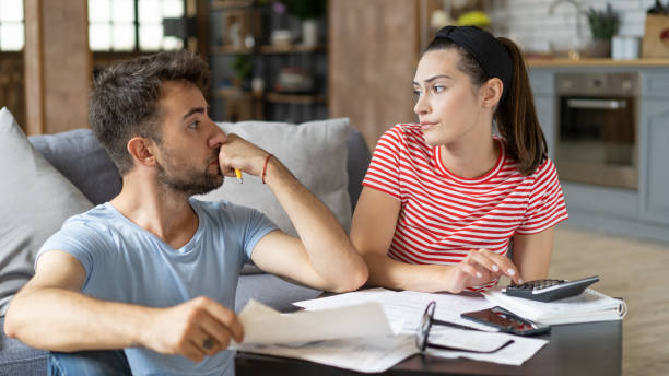 Frustrated concerned young couple calculating overspend budget, doing paperwork job at laptop, talking about financial problems, insurance, mortgage, fees, loan conditions, bankruptcy, economic inflation stock photo