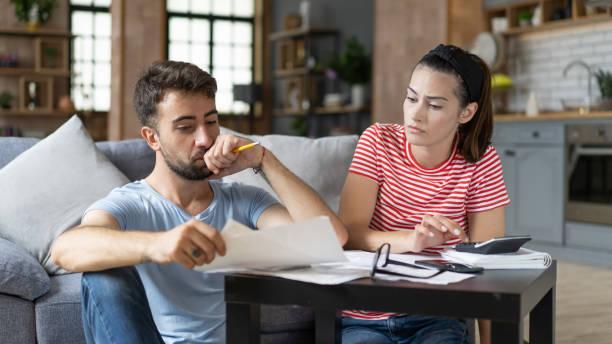 Frustrados preocupados jovem casal calculando orçamento de gastos excessivos, fazendo trabalho de papelada no laptop, falando sobre problemas financeiros, seguro, hipoteca, taxas, condições de empréstimo, falência, inflação econômica - foto de acervo