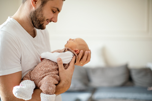 Newborn baby sleeping in her father's arms at their home. Father is handsome young man