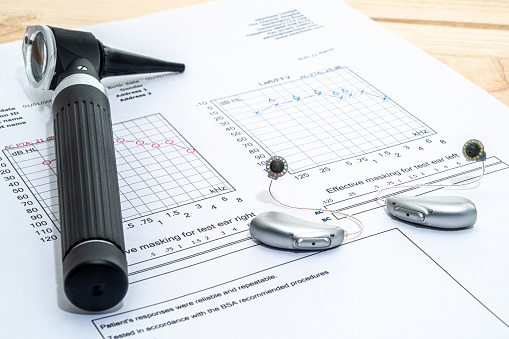 Hearing aids and an otoscope placed on an audiologists desk with an audiogram hearing test chart