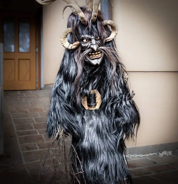 Portrait of a boy in a krampus costume, black goat skin, horns and a wooden mask, Austria, Salzburg. High quality photo
