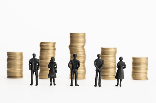 Group of figurines looking at stacks of coins. White background. Copy space. Business or economy concept