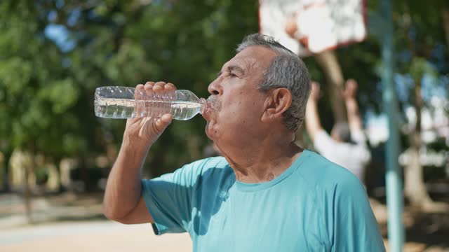 Senior man drinking water at the basketball court
