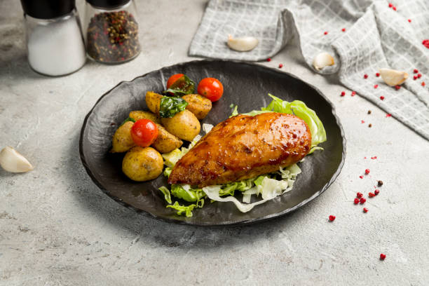 istock Grilled chicken Breasts with mini potatoes and tomatoes on black plate on grey table 1450407348