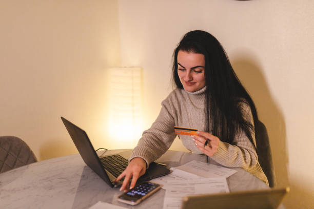 istock Happy young woman paying bills at home using her laptop 1450412612
