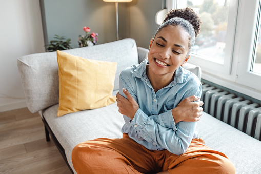 Beautiful young woman sitting on the sofa at home in the morning and hugging self