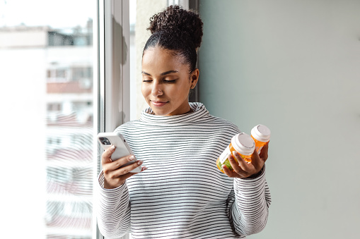 Una joven feliz que sostiene un teléfono inteligente y un frasco de pastillas photo