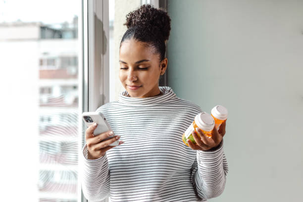 молодая счастливая женщина держит смартфон и бутылку с таблетками - pharmaceutics стоковые фото и изображения