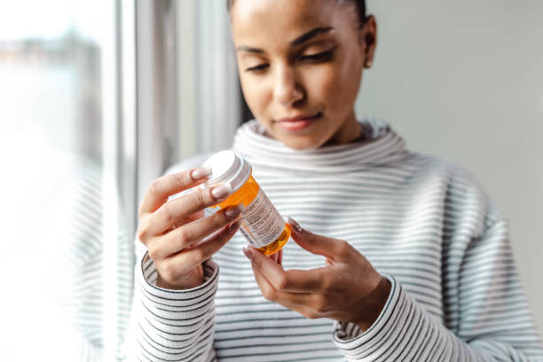 eine ernste junge frau hält eine flasche medikamente in der hand - prozac stock-fotos und bilder