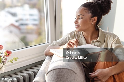 istock Young African American woman writing a diary and thinking 1450422183