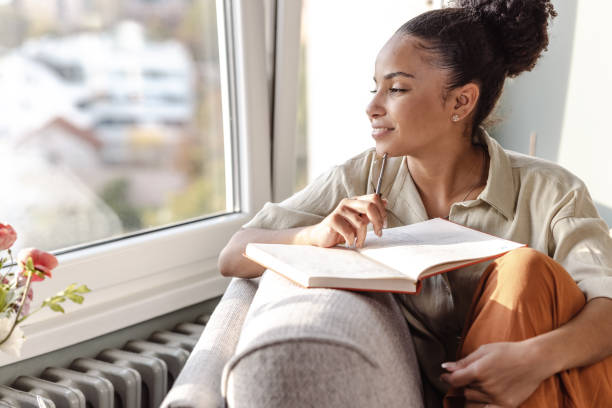 Young African American woman writing a diary and thinking stock photo