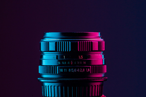 Retro camera lens on black background, shot with turquoise and pink gel lighting