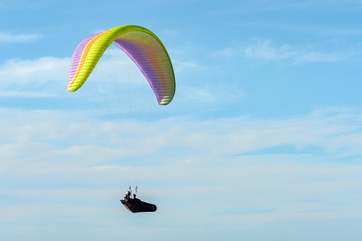 Multi colored paraglider flying in the sky on a beautiful blue sky with clouds. Copy space on right side for text