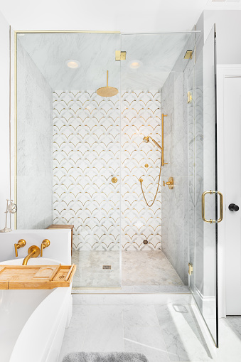 A beautiful tiled shower and tub with gold and white tiles on the walls, mosaic marble tiles on the floor, and gold shower head and hardware.