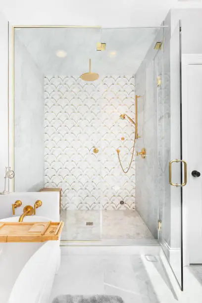 A beautiful tiled shower and tub with gold and white tiles on the walls, mosaic marble tiles on the floor, and gold shower head and hardware.