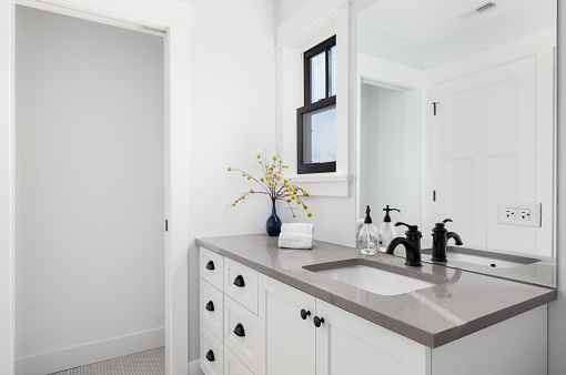 A beautiful white bathroom with cozy decor on the granite counter top, black faucet and window frames, and tile flooring.