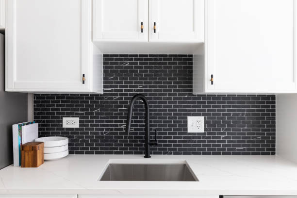 istock A kitchen sink detail with white cabinets and a black subway tile backsplash. 1450445653