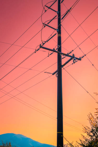 Power poles and lines, or electricity pylons and cables at sunset, abstract geometry of the shapes and lines against a moody sunset sky stock photo