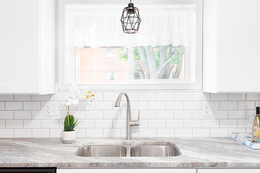 Horizontal image of modern kitchen detail. Showing a kitchen sink and faucet with water running from the faucet, and potted herbs behind on window sill. Space for copy.