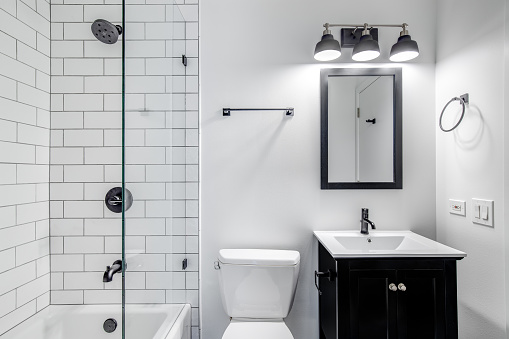 A small modern bathroom with a dark vanity, mirror frame, and hardware. White subway tiles line the bathtub and shower with black faucets.