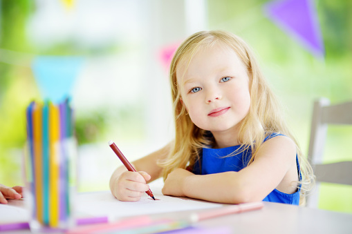 Cute little girl drawing with colorful pencils at a daycare. Creative kid painting at school. Girl doing homework at home.