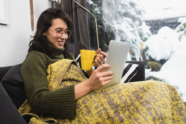 istock Happy young woman warming under the blanket and using tablet 1450456366