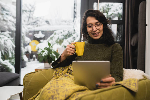 istock Happy young woman warming under the blanket and using tablet 1450456369