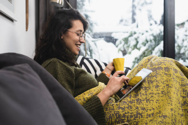 istock Happy young woman enjoying coffee under the blanket and using tablet 1450456371