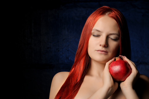 portrait of beautiful girl with red hair and pomegranate fruit on the background of blue wall. different poses.