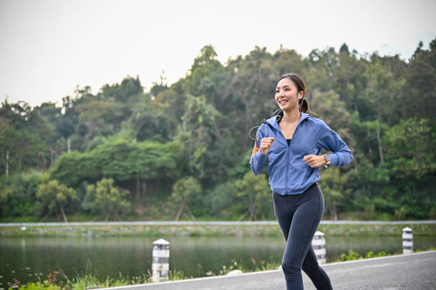 Happy Asian woman listening to music while enjoys running at the park in the morning. stock photo